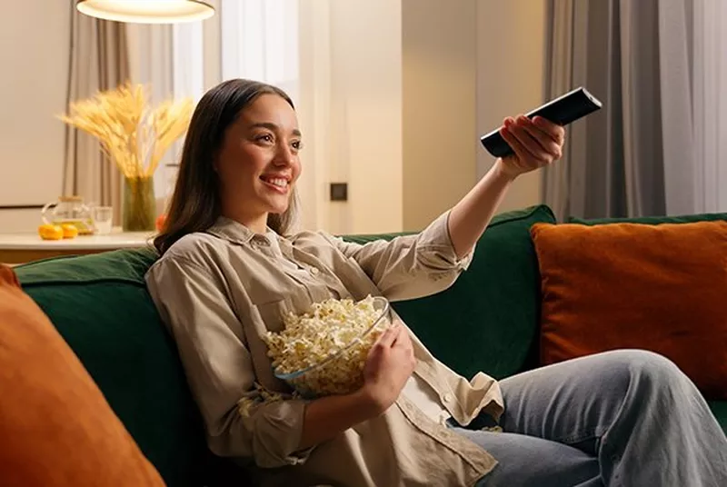 a woman sitting on a couch holding a bowl of popcorn and a remote control